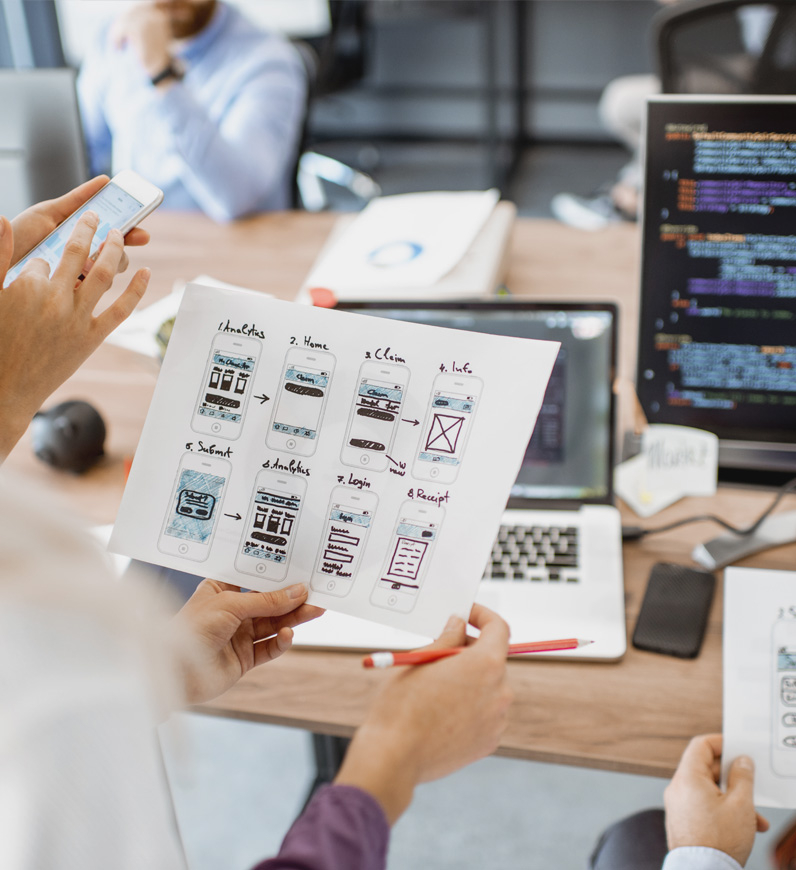 A team of designers and developers working on a laptop in an office setting, focusing on mobile development production service.