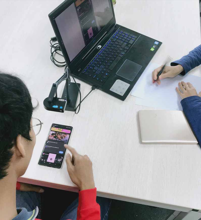 Two people conducting usability testing at a table with a laptop and a phone, identifying problems and bugs to improve business goals.